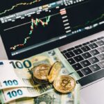 Bitcoin and Euro notes on laptop keyboard with stock market graphs in Berlin, Germany.